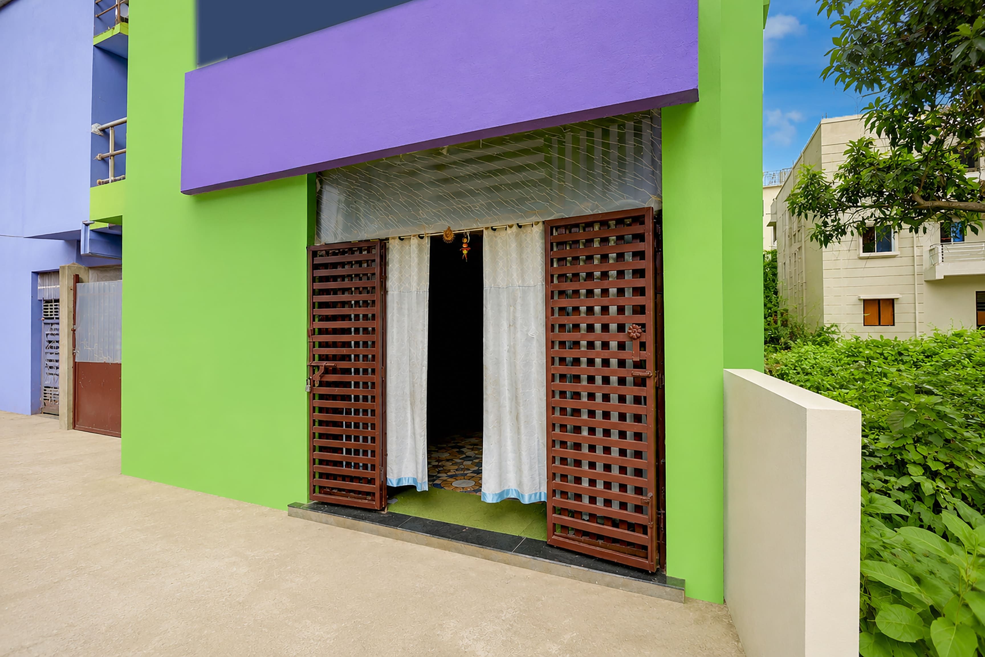 Un edificio con fachada verde, sección superior morada y una ventana con persianas marrones.