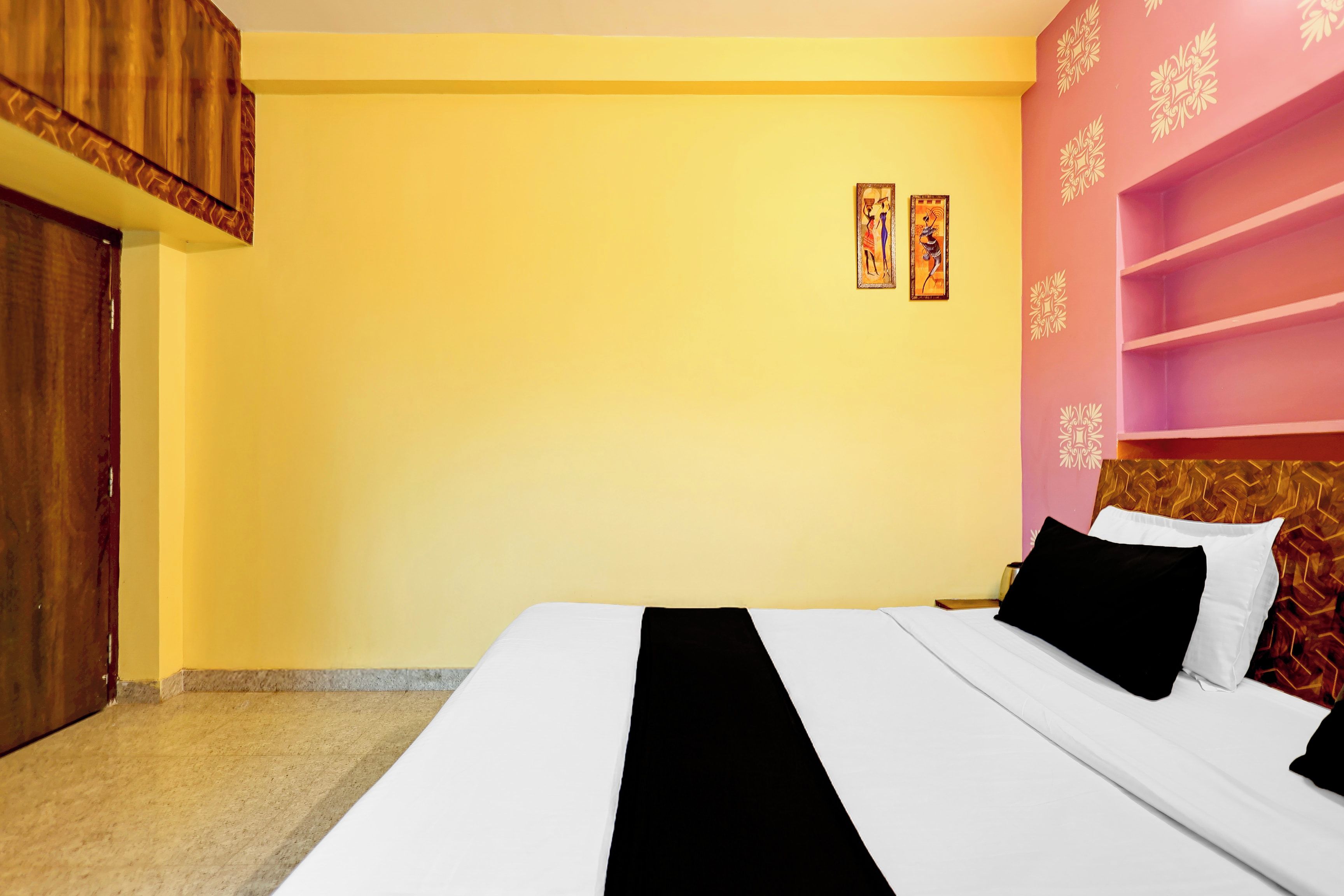 A hotel room with a bed, a wooden wardrobe, and a pink wall with decorative patterns.