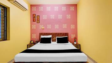 Una habitación de hotel con una cama, una mesita de noche, un aire acondicionado de pared y una ventana con barrotes.
