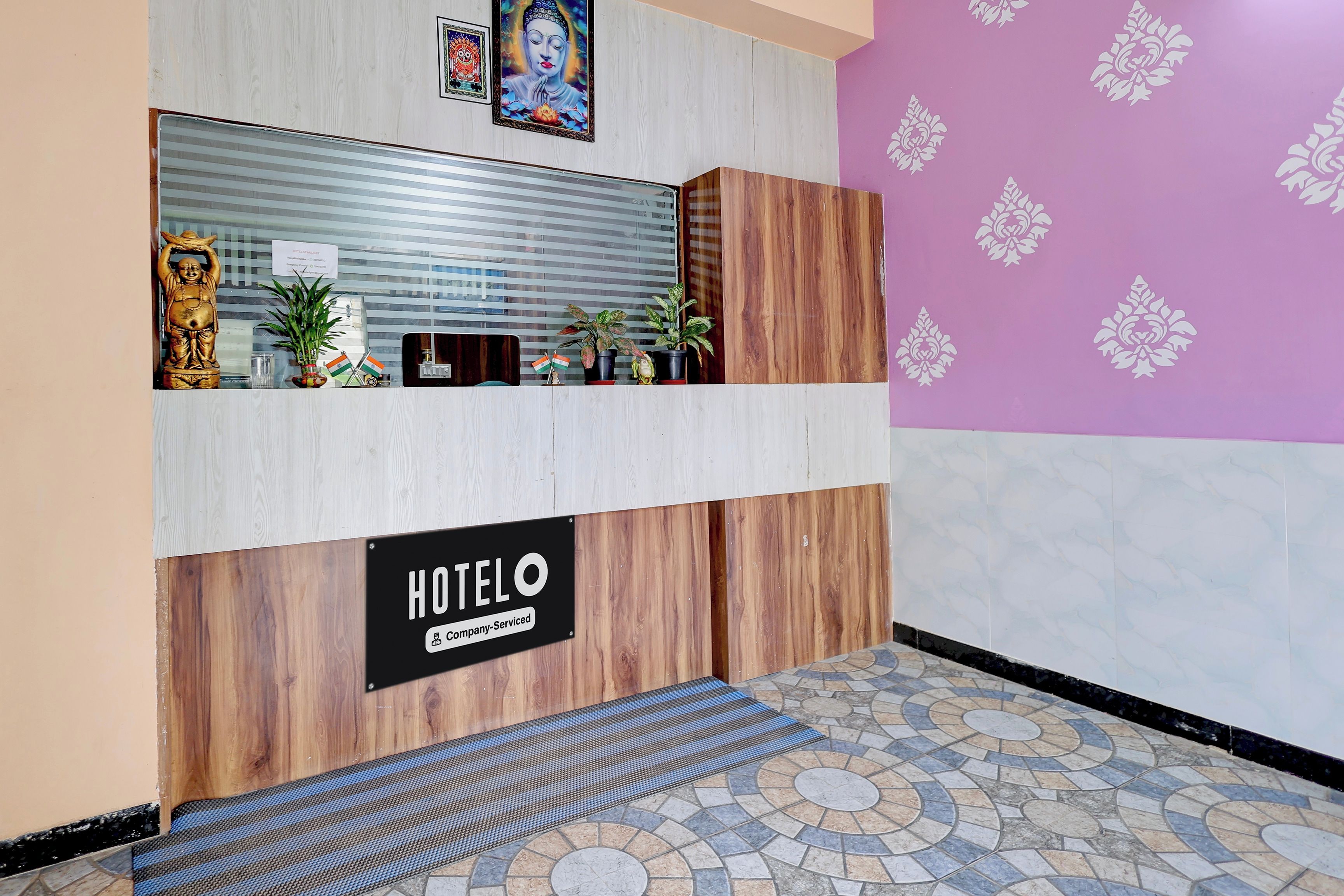 Una mesa de recepción con un cartel que indica que es un hotel de servicio empresarial. Hay plantas en macetas y una estatua sobre el mostrador.