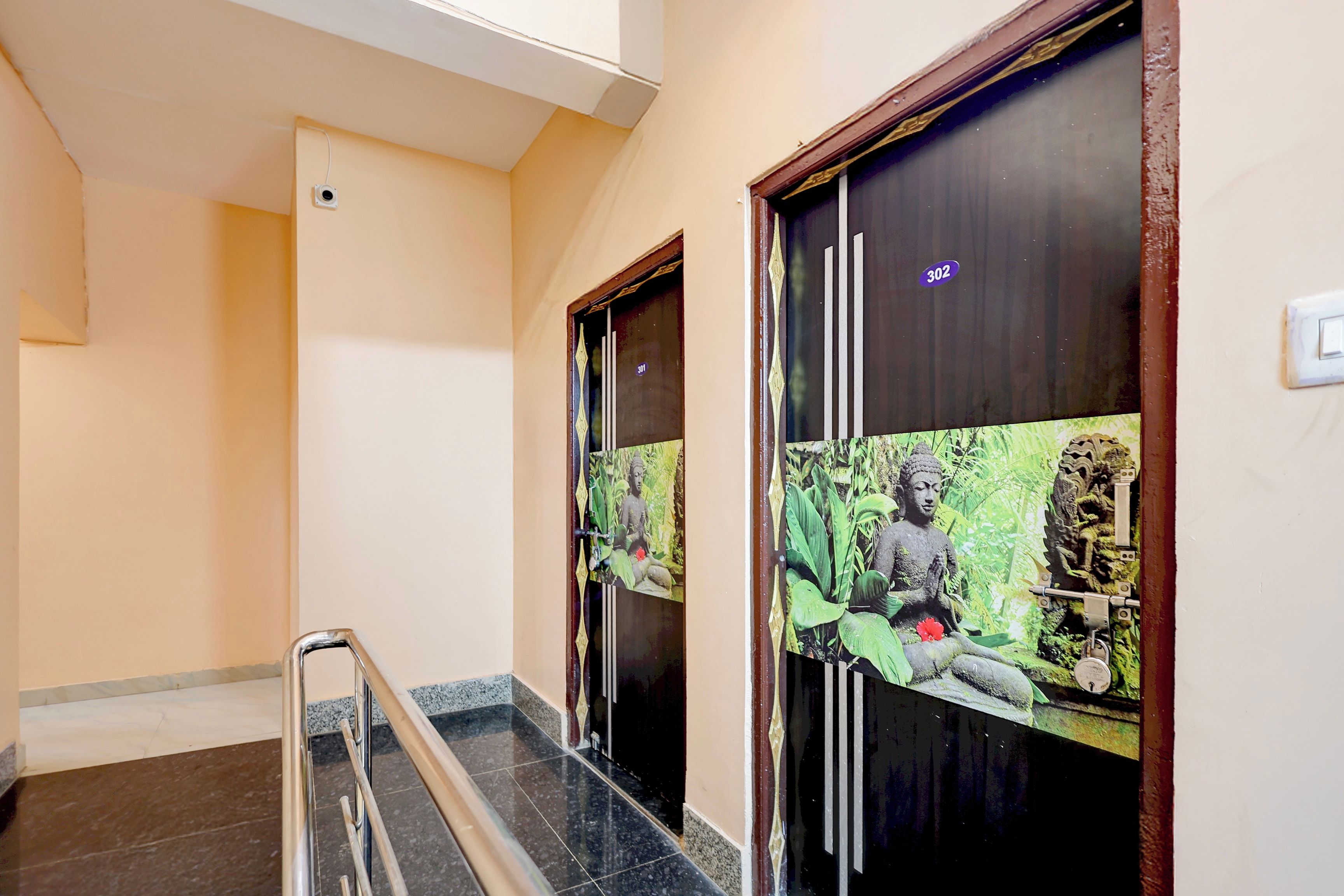 A hallway with a marble floor, a metal handrail, and doors with a Buddha statue and greenery design.