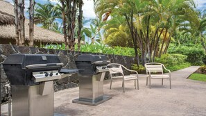 Two barbecue grills, a stone wall, and two chairs in a tropical setting.