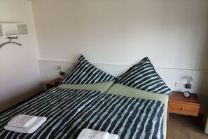 A bed with striped bedding, two pillows, a bedside table with a lamp, and a wall-mounted light fixture. - Holiday apartment Strandhaus (Norderney)