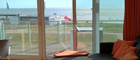 A room with a large sliding glass door leading to a balcony with a view of the sea.