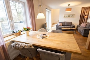 A modern living room with a wooden dining table, grey sofas, and a staircase leading to an upper floor. - Holiday home in Brilon with swimming pool (Brilon)