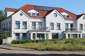 A multi-story residential building with a red-tiled roof, balconies, and a well-maintained garden. - Holiday apartment with 2 bedrooms (Norderney)