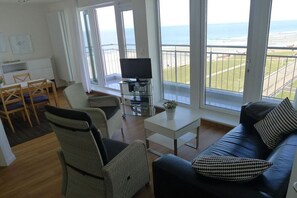 A living room with a sofa, chairs, a coffee table, and a TV. There is a balcony with a view of the sea. - Holiday apartment with 2 bedrooms (Norderney)