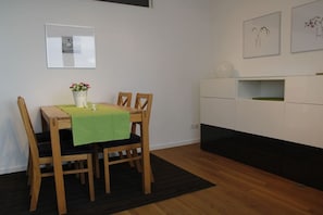 A dining area with a wooden table, four chairs, a green tablecloth, and a vase with flowers. - Holiday apartment with 2 bedrooms (Norderney)