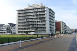 A multi-story building with balconies, a paved walkway, and a grassy area. - Holiday apartment with 2 bedrooms (Norderney)