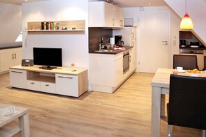 A modern kitchen with white cabinetry, a built-in TV, and a dining area with a table and chairs. - House Hahnen - Upper Floor (Norderney)