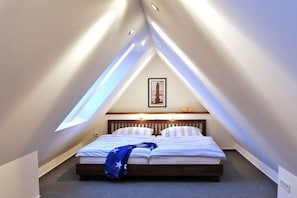 A bedroom with a sloped ceiling, a bed with a blue blanket, and a framed picture on the wall. - House Hahnen - Upper Floor (Norderney)