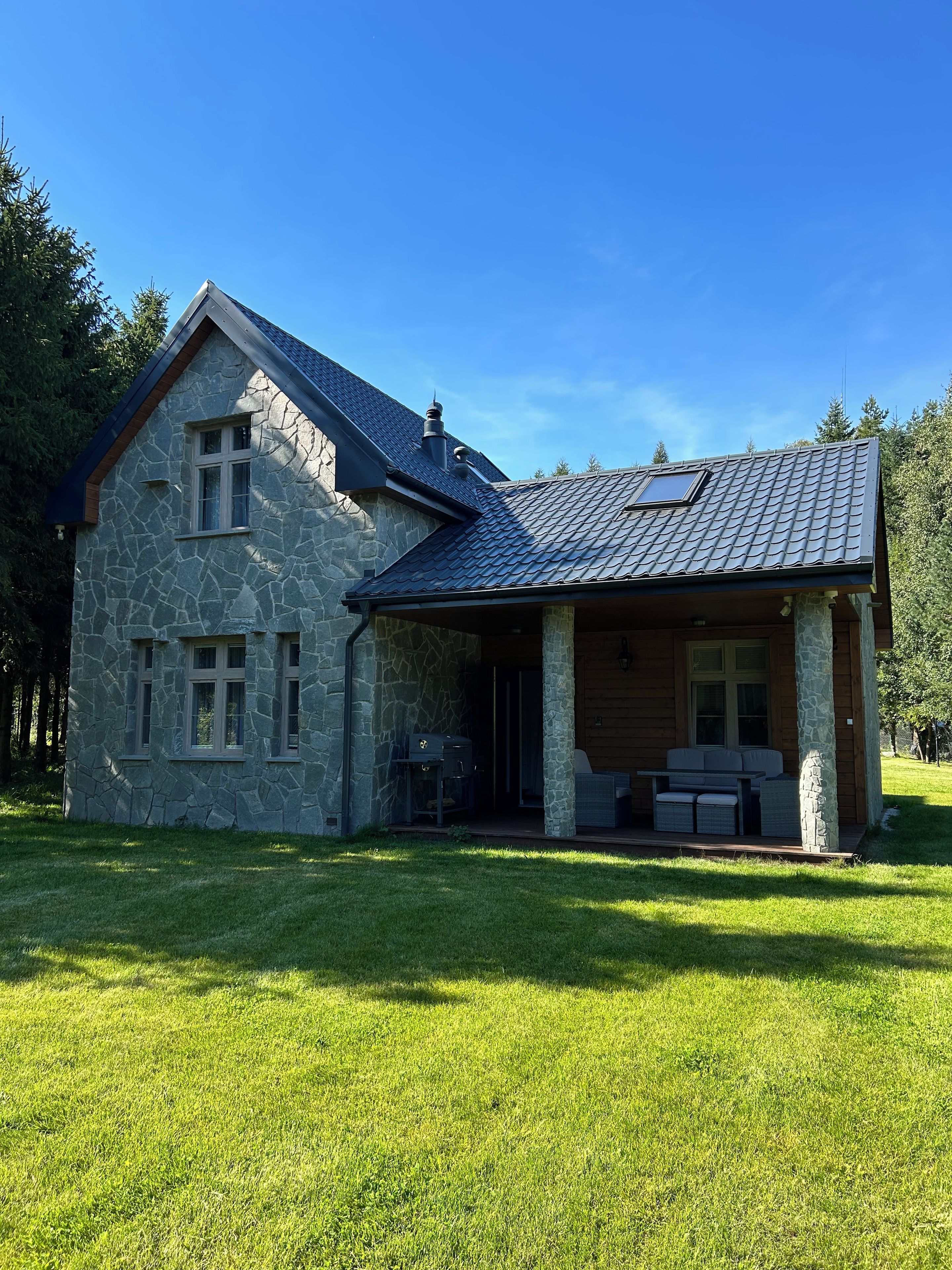 Une maison en pierre avec un toit en pente, une véranda et une pelouse.