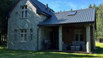 Une maison en pierre avec un toit en pente, une véranda et une pelouse.