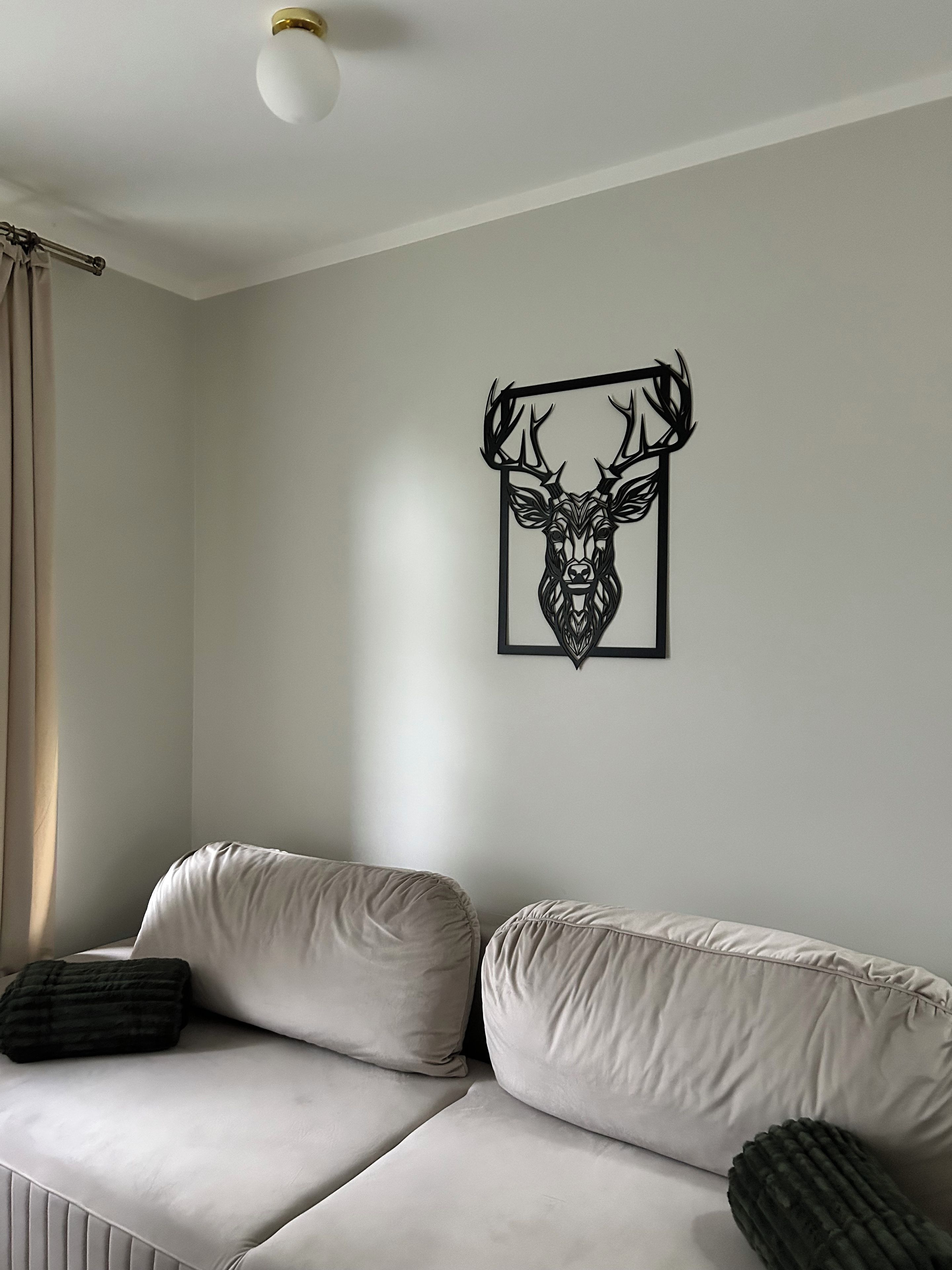 Une pièce avec un canapé blanc, une œuvre d’art représentant une tête de cerf encadrée au mur et un luminaire au plafond.