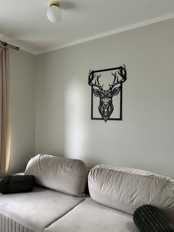 A room with a white sofa, a framed deer head artwork on the wall, and a ceiling light.