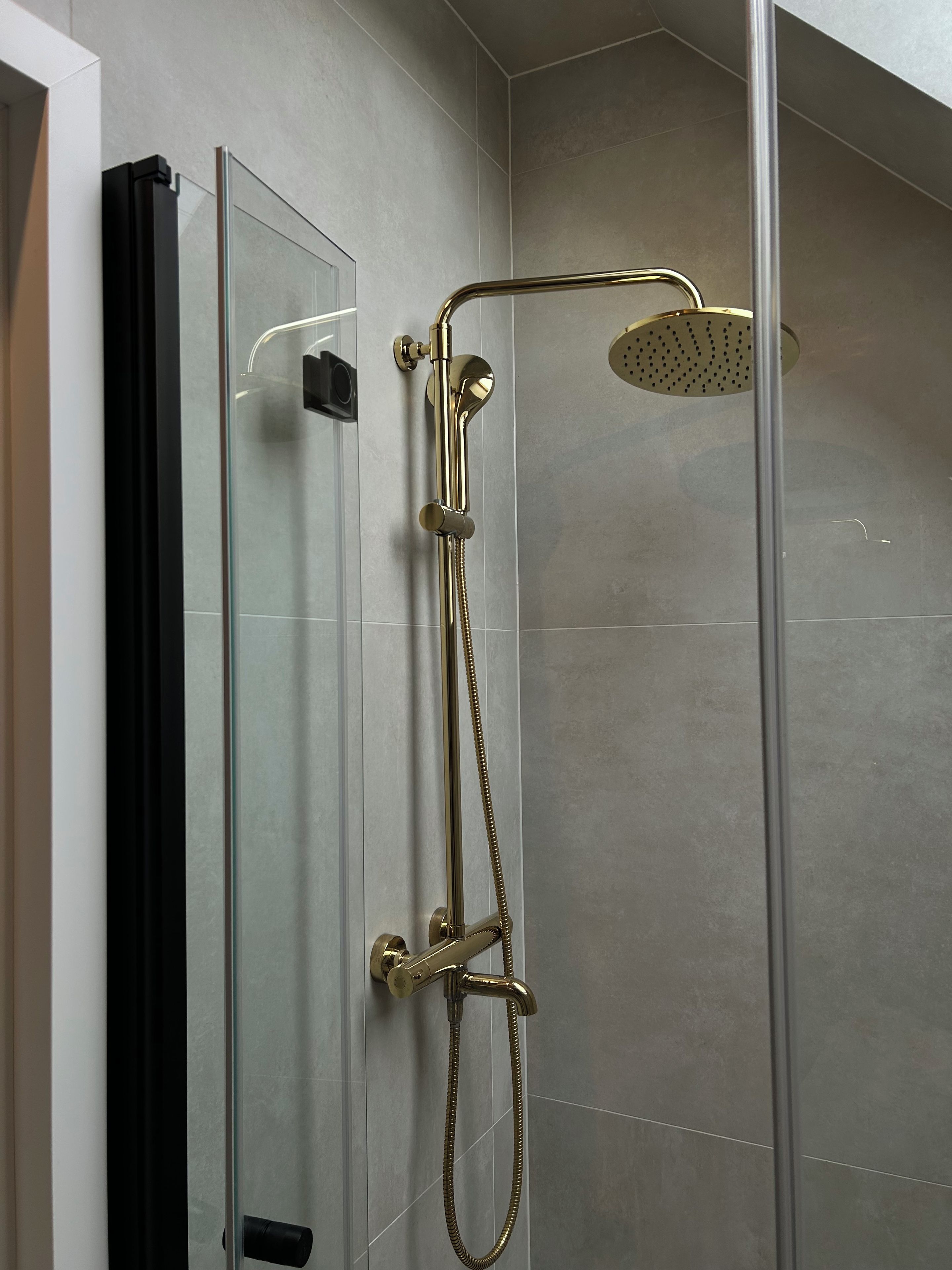 A modern bathroom with a glass shower enclosure, a handheld showerhead, and a wall-mounted faucet.