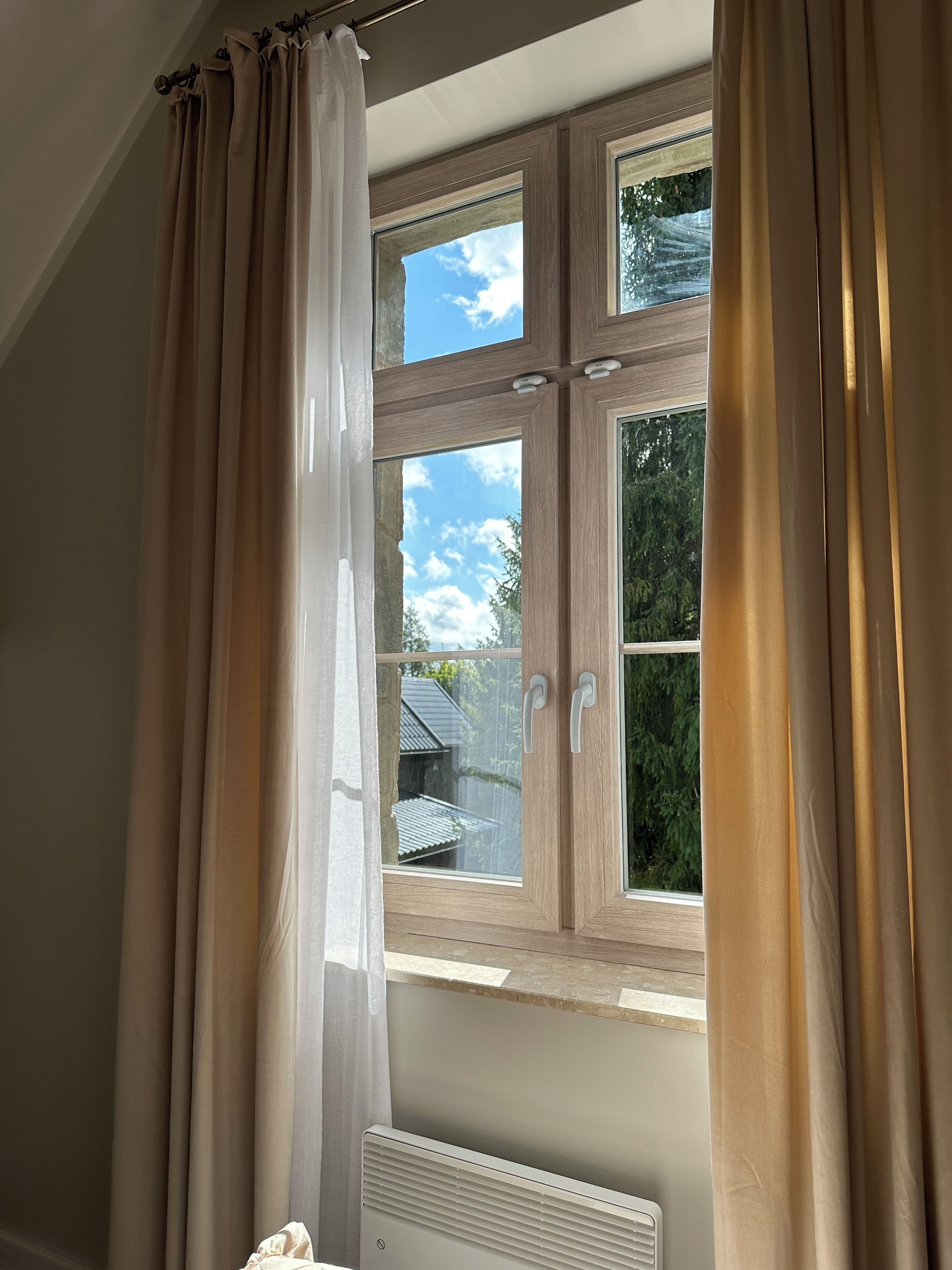 Une fenêtre donnant sur une maison et des arbres, avec des rideaux et un radiateur.