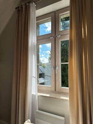 Une fenêtre donnant sur une maison et des arbres, avec des rideaux et un radiateur.