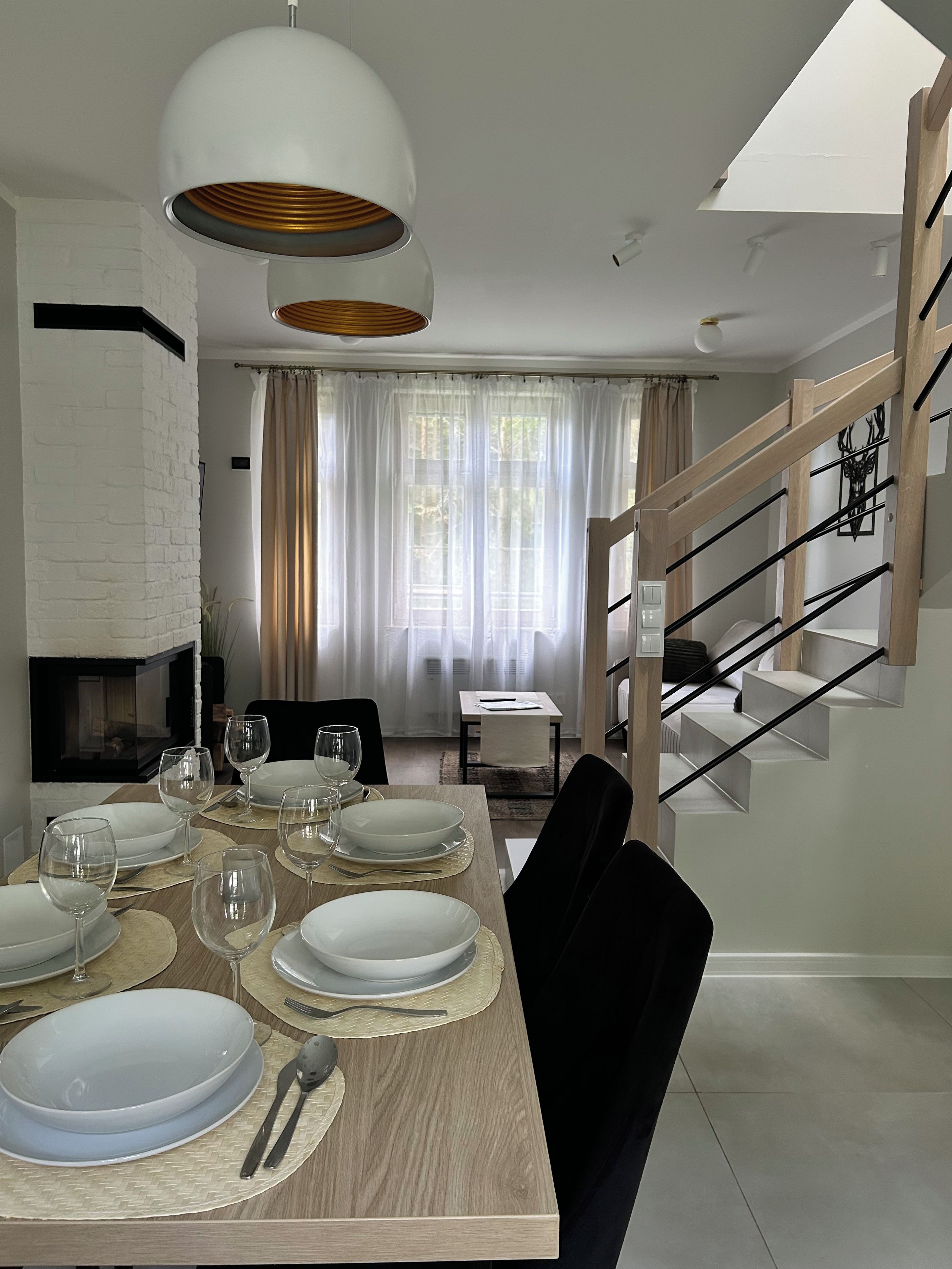 Un espace de repas moderne avec une table en bois dressée pour six personnes, un escalier avec des rampes en bois et un mur en briques blanches.