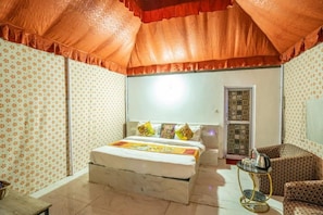 A room with a bed, a small table, a chair, and a patterned wall. - The Gujarat Capital Resort (Jaisalmer)