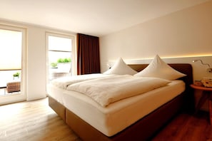 Ein Hotelzimmer mit einem großen Bett, einem Nachttisch mit Lampe und Blick ins Freie durch eine Schiebetür.