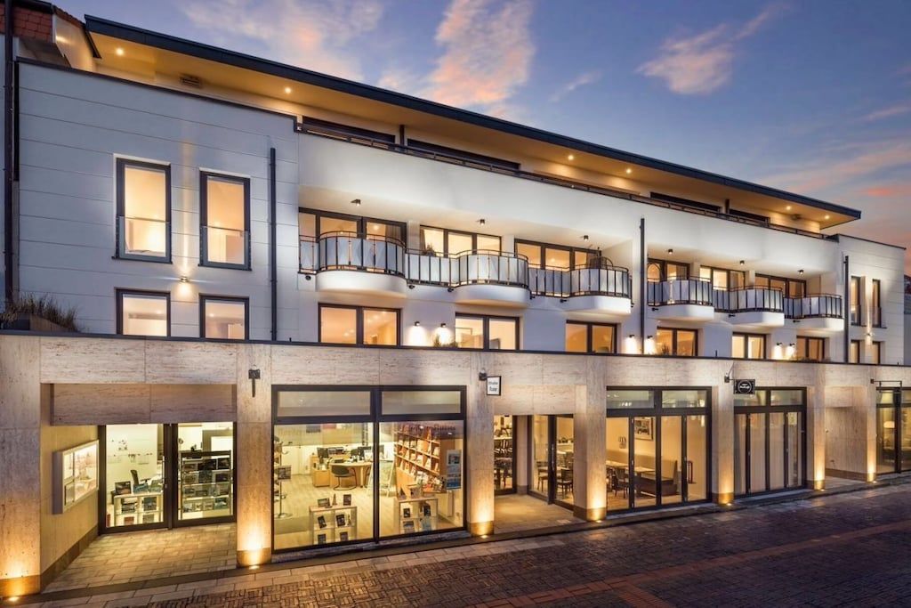 Un hôtel moderne doté de nombreux balcons, de grandes baies vitrées et d’une façade bien éclairée.