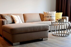 A modern living room with a sofa, pillows, and a metal side table. - Passepartout 1st floor / 2 bedrooms (Norderney)