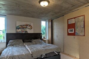 Un dormitorio con cama, cabecera, ventana y pared con mapa y cartel.