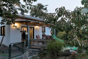 A house with a covered porch, a barbecue grill, and a garden with various plants and a tree. - Holiday home in Bell with swimming pool (Bell)