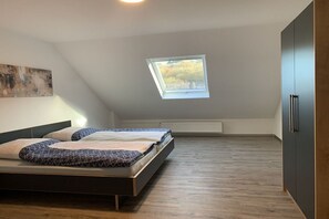 Ein Schlafzimmer mit geneigter Decke, einem Oberlicht, einem Bett mit gemusterten Betttextilien und einer Heizung.