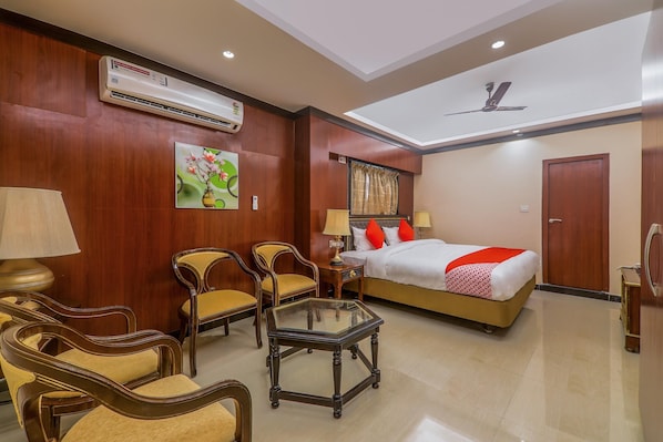 Habitación de hotel con cama, dos sillas, una mesa, equipo de aire acondicionado y ventilador de techo.