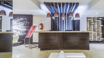 Un área de recepción moderna con piso de mármol, una recepción y un extintor de incendios en la pared.