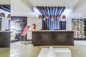 Un área de recepción moderna con piso de mármol, una recepción y un extintor de incendios en la pared.