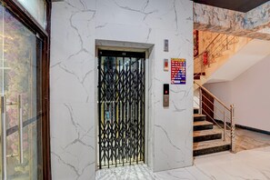 Ein Aufzug mit einem schwarzen Metallgitter, einem Brandmelder und einer Treppe mit einem roten Feuerlöscher.