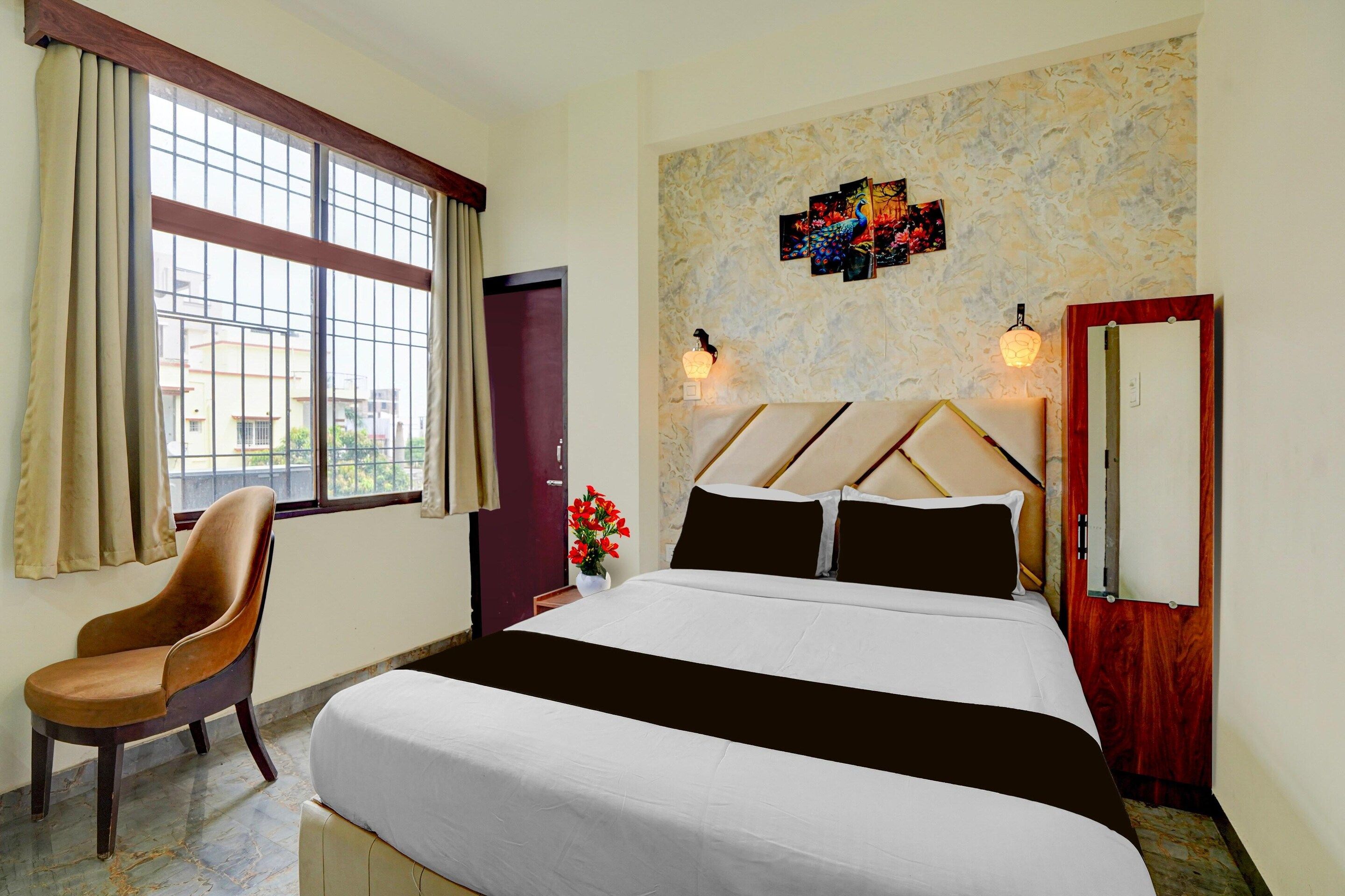 A hotel room with a bed, a chair, a window with curtains, a wall-mounted lamp, and a door.