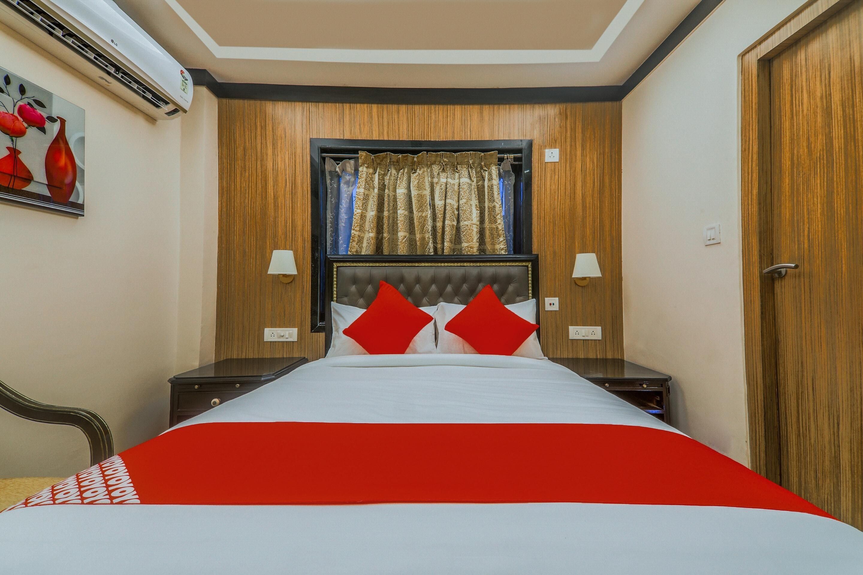 A hotel room with a bed, a window with curtains, a wall-mounted air conditioner, and a door.