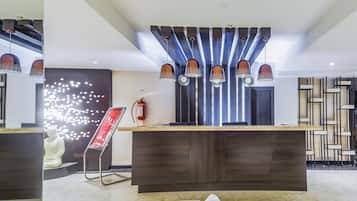 A modern reception area with a marble floor, a reception desk, a fire extinguisher, and a decorative wall piece.