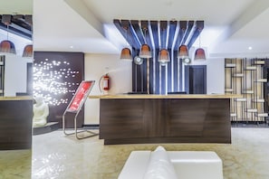 Una zona de recepción moderna con suelo de mármol, un mostrador de recepción, un extintor y un elemento decorativo en la pared.