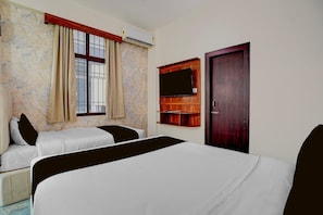 Habitación de hotel con dos camas, una ventana con cortinas, un equipo de aire acondicionado, una puerta de madera y un televisor montado.