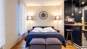 Een slaapkamer met een bed, nachtlampen, een wandklok en een kitchenette.