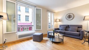 A modern living room with a grey sofa, a round coffee table, and a large window with a view of a balcony. - Paris - Bastille l AC & 10 min from Marais (Paris)