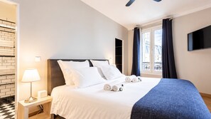 A hotel room with a bed, a nightstand, a lamp, a window with curtains, and a TV on the wall. - Paris - Bastille l AC & 10 min from Marais (Paris)
