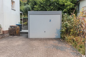 A gated area with a metal shed, a trash bin, and a staircase leading to a building. - Cozy house surrounded by beautiful nature, with a garden and parking (Obernhof)