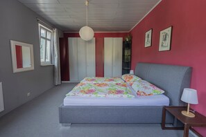A bedroom with a bed, a nightstand, a lamp, a window, and a door.