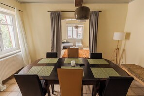A dining area with a table set for four, chairs, a lamp, and a view of a bedroom with a bed and window.