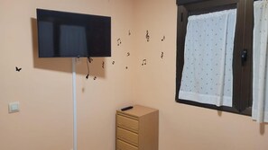 Una habitación con un televisor montado en la pared, una ventana con cortina y un mueble de madera.