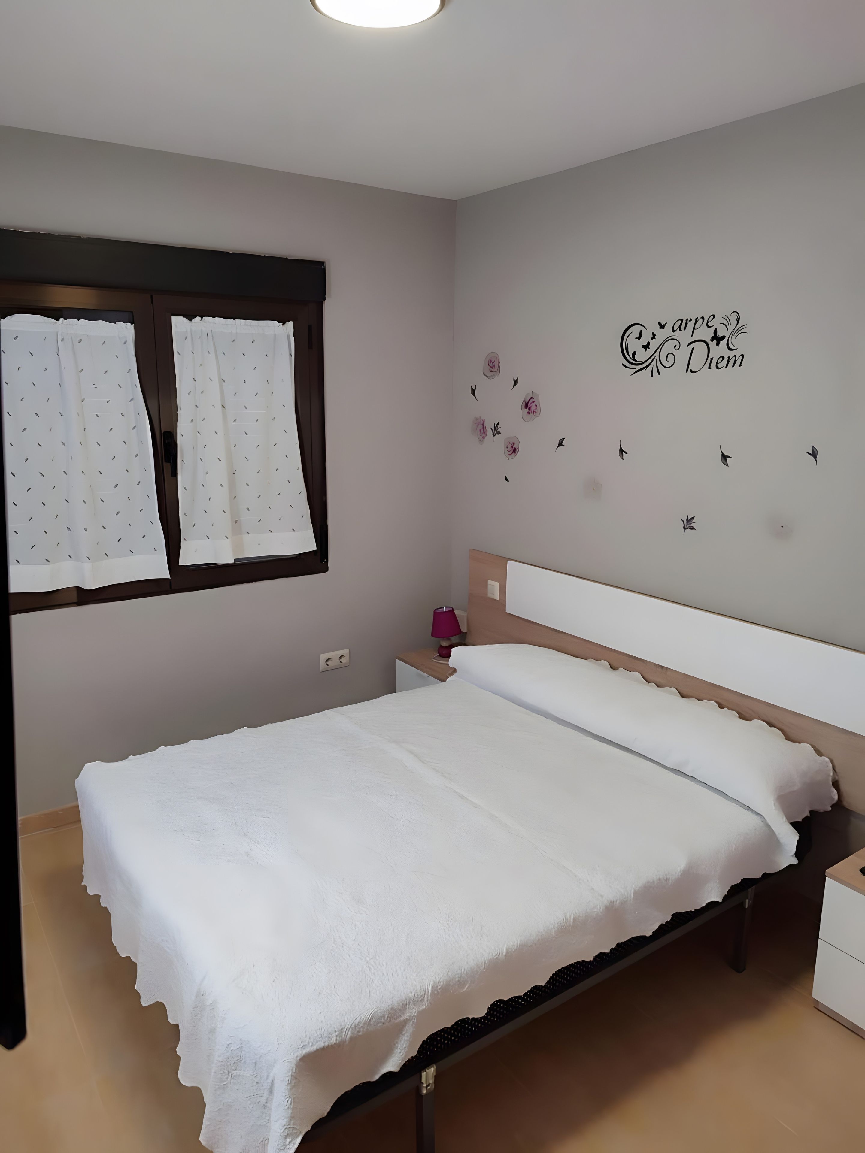 A bedroom with a bed, a nightstand, a wall decoration, and a window with curtains.