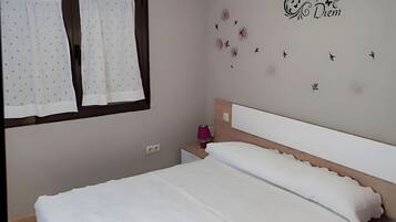 A bedroom with a bed, a nightstand, a wall decoration, and a window with curtains.