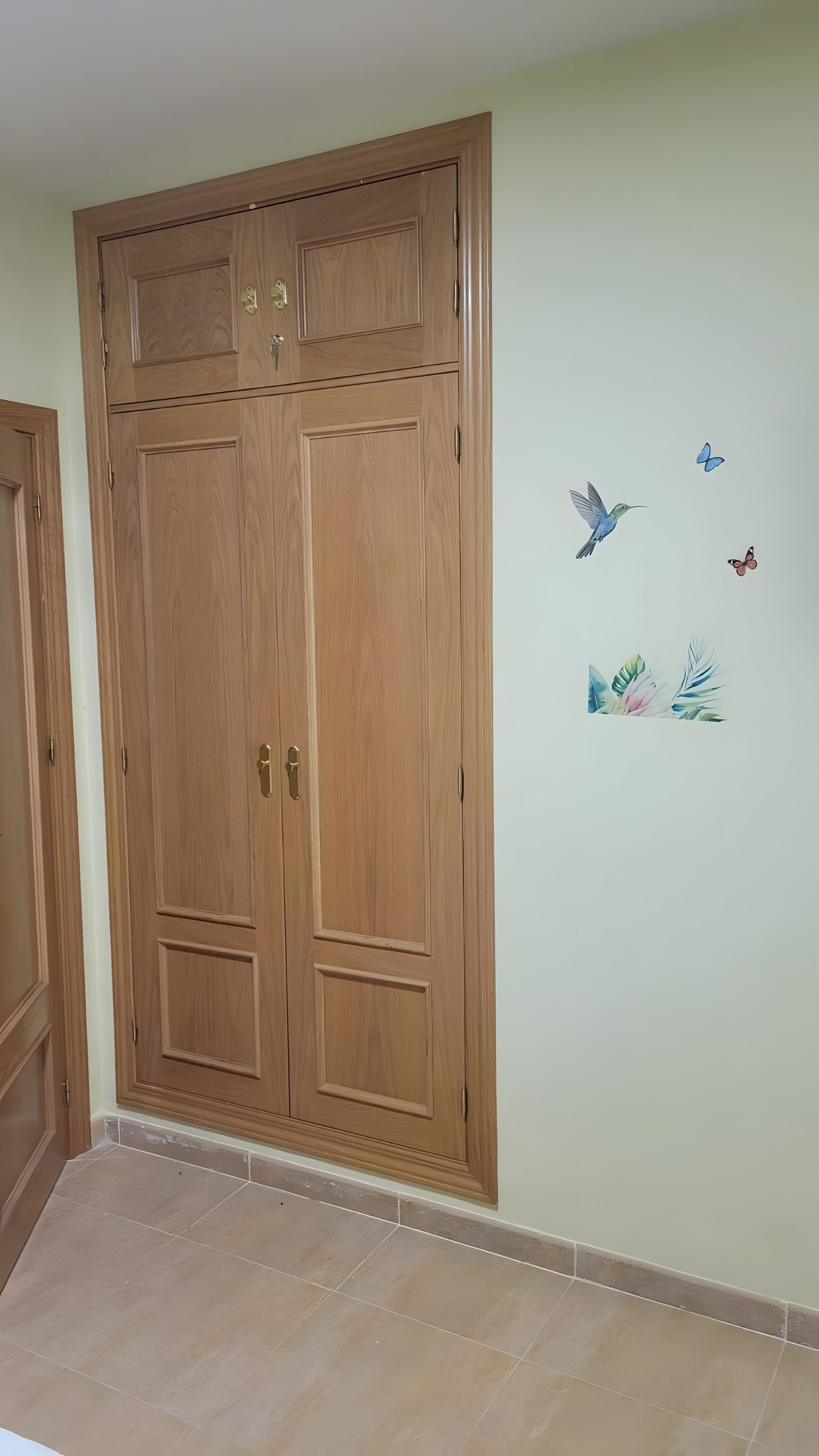 Une pièce avec une armoire en bois, un sol carrelé et des autocollants décoratifs représentant un colibri et des papillons.