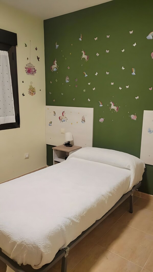 Habitación individual con una pared verde, una mesita de noche, una lámpara y adhesivos de mariposas.